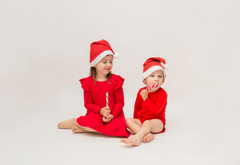 Obraz premium little girl and boy in red caps with lollipops on a white background with a copy of space