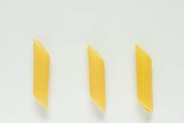 Close up of three single Penne noodles on white backgorund; italian pasta