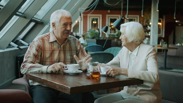 Smiling man and woman of old age are talking and drinking tea enjoying leisure time together in modern cafe. Conversation and happy family concept.