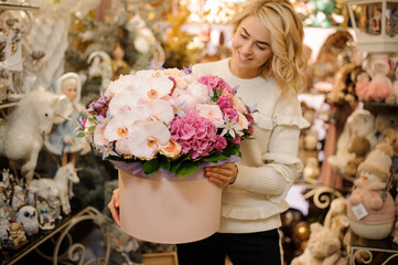 elegant composition of fresh flowers in round pink box in hands of smiling woman