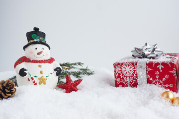 christmas card with snowman, red gift box, fir branches and cones in the snow. copy space..