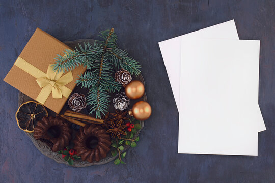 Christmas composition. Gift with toys, chocolate muffin, spices, spruce branch and berries on a metal vintage plate, silver spoon, cup of coffee with cinnamon and empty congradulation card on the tabl