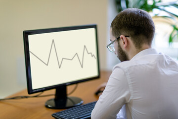 A man with glasses sits at the monitor, looks at the graph