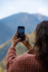 a girl takes photos of a mountain lake on her mobile phone