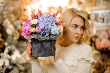 blonde woman holds composition with flowers of hydrangea rose and peony in her hands.
