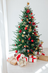 Big beautiful christmas tree decorated with beautiful shiny baubles and many different presents on wooden floor.