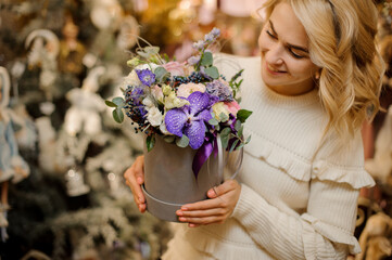 bright arrangement of white and purple flowers in round box in hands of blonde woman
