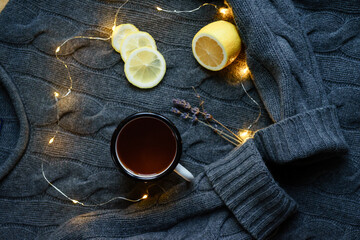 Obraz na płótnie Canvas a cup of tea, lights and lemon on a gray sweater background. the concept of tranquility, warmth and comfort. hygge at home