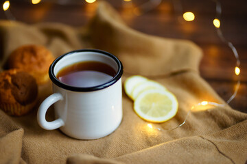 a cup of tea, lights and lemon on a beige sweater background. the concept of tranquility, warmth and comfort. hygge at home