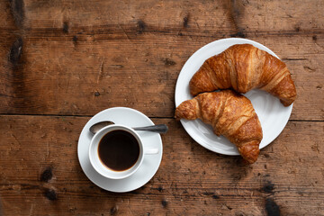 breakfast on wooden table with two croissants and cup of coffee. view from above