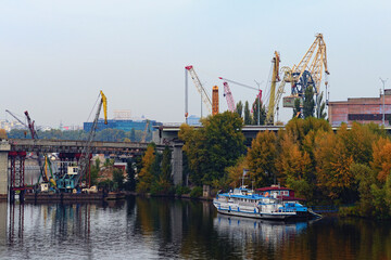 Fototapeta premium Close-up view of the process of unmounting an old bridge to the Rybalskyi Island (or Peninsula). Heavy cranes are used to dismantle bridge structures. Old crane booms in the background