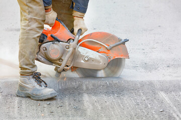 The builder cuts the old asphalt with a portable petrol cutter and a diamond cutting disc, creating...