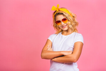 Cool little blonde girl. Charming teenage kid girl in fancy sunglasses grinning and posing for the camera isolated over pink background.