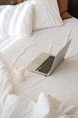 there is a laptop on the bed, next to it lies a bouquet of flowers and a mug of coffee