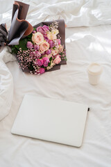 Obraz na płótnie Canvas there is a laptop on the bed, next to it lies a bouquet of flowers and a mug of coffee