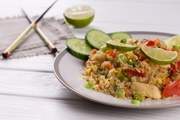 Khao Pad, fried rice with vegetables, meat and eggs, with fresh cucumbers, tomatoes, with chopsticks.