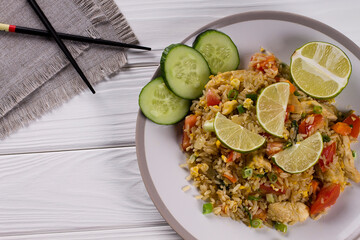 Khao Pad, fried rice with vegetables, meat and eggs, with fresh cucumbers, tomatoes, with chopsticks.