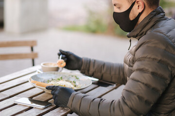 Fototapeta premium Man in black face mask sitting in cafe and prepared for eating vegan salad. Quarantine cafe concept. Covid-19