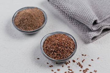 Brown flax seed and ground or crushed flaxseed or linseed in small bowl on light gray background.