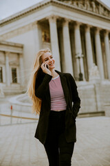 Fototapeta premium Beautiful smiling woman using mobile phone and walking ba Austrian Parliament in Vienna, Austria