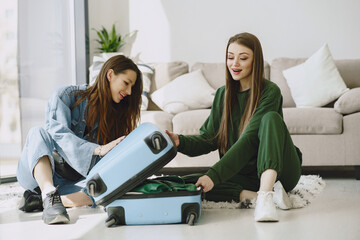 Excited women trying to close full suitcase. Packing luggage. Travel, lifestyle and vacation concept.
