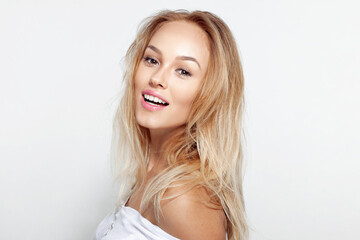 Fototapeta premium Portrait of smiling blonde young woman with beautiful natural makeup ang long wavy hair, over white background.