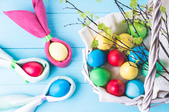 Easter eggs in the shape of rabbit ears, a basket with colorful Easter eggs and tree branches with green leaves, on a blue wooden background, selective focus, tinted image