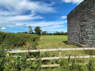Looking over a wooden fence, past an old stone barn, into farmland in, Bolton by Bowland, Clitheroe, UK
