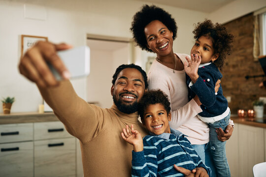 Happy black parents with kids making video call over smart phone at home.