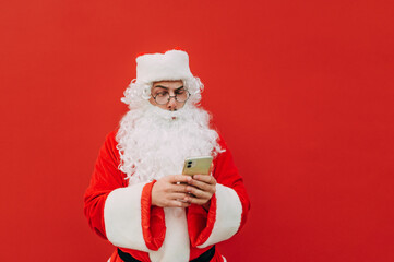 Concentrated Santa Claus is frowning his eyebrows when using a smartphone. Serious Santa is attentive when using a mobile phone device.
