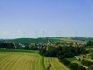 Large wind turbines to generate electricity on a field in Germany. Nice little town. Settlement in Europe. - 395604797