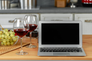 Laptop and glass of red wine on wooden kitchen table