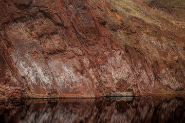 A cliff of red rock near a lake with black water