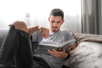 young man lying on a sofa, reads a book