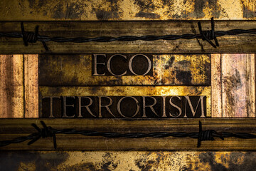 Eco Terrorism text message lined with barbed wire on textured lead grunge copper and vintage gold background