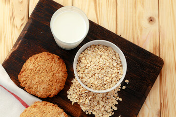 Oat cookies with oat flakes and cup of milk on wooden table