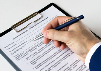 A man's hand with a pen signs a contract in a folder