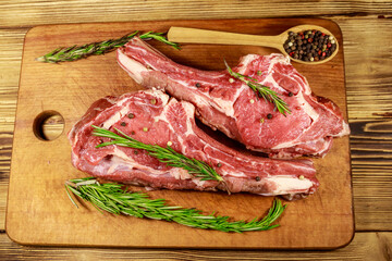 Raw fresh beef rib eye steaks on bone with spices and rosemary on wooden table. Top view