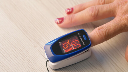 Adult woman sticks her finger into a pulse oximeter. A girl checks the pulse and oxygen level in...