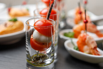 Cherry tomatoes and mozzarella canapes on skewers in a glass glass with a background of king prawns in close-up