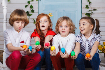 Children holding easter eggs. Beautiful children sit near the basket with tulips and hold Easter eggs in their hands. Funny moments