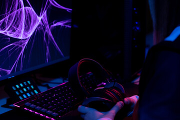 purple, blue and pink set up gamer with a keyboard and monitor belonging to a girl who holds her headphones in her hands