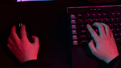 Detail of a gamer girl's hands using her computer keyboard blue and pink LEDS lights