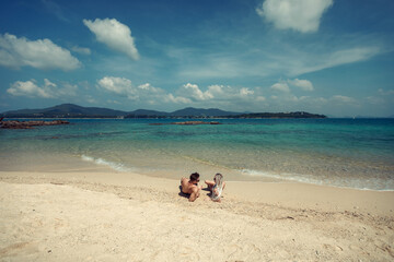 Sensual young couple in swimsuits laying on the sand by the sea over sky and tropical island background. Phuket. Thailand.
