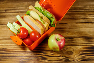 Apple and lunch box with sandwiches and fresh vegetables on a wooden table