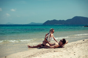 Sensual young couple in swimsuits laying on the sand by the sea over sky and tropical island background. Phuket. Thailand.