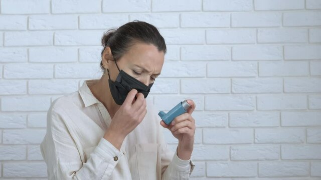 Suffer from allergy attack. A woman in medical facial mask has a seasonal asthma attack. A stressed female use an inhaler to cure.