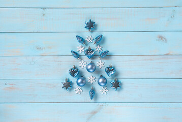 Christmas light blue background. Festive decoration with blue and silver baubles, hearts, snowflakes, stars, cones in Christmas tree shape arranged on rustic pastel blue wooden table, top view.