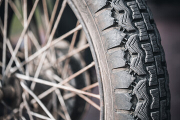 Old or vintage tyre on motorcycle wheel. Cracked rubber on metal rim. Wheel spokes.