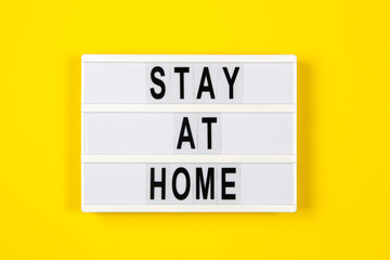White lightbox with text STAY AT HOME on yellow background. Healthcare, medical, quarantine concept. Top view, copy space